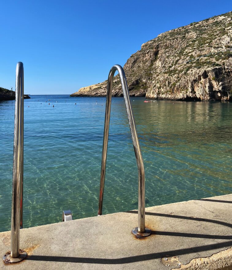 Xlendi Bay with cliffs, calm water, and swimming ladders.